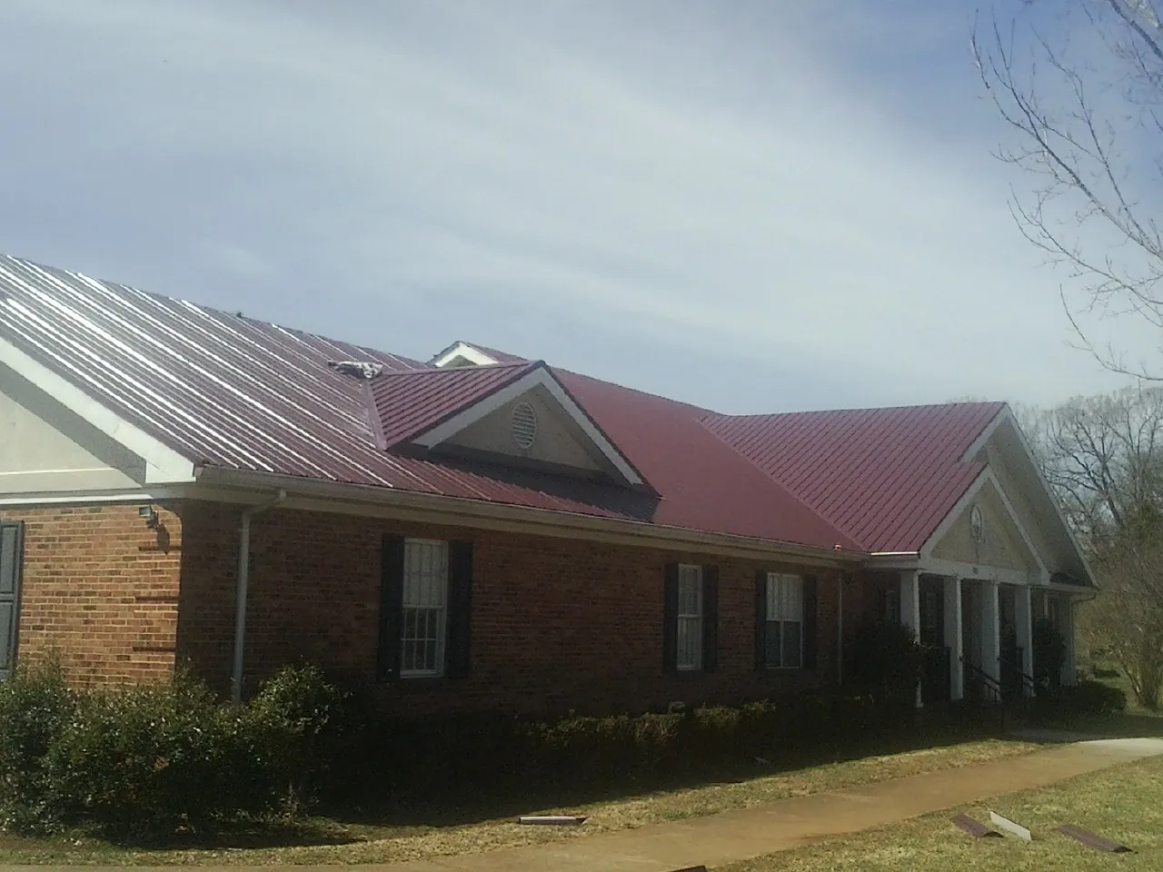 Red metal roof with gabled entries on a long brick building, from a Hail Damage Roof Repair job in Klamath River