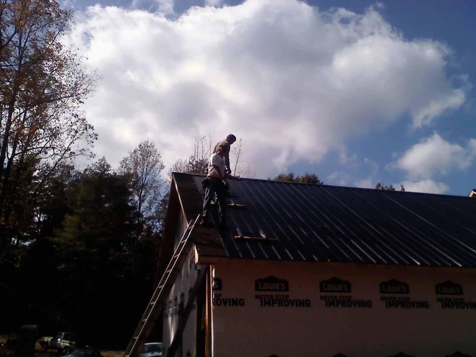 Roofer fastening dark metal panels high against a cloudy sky, from a Roof Inspection job in Klamath River