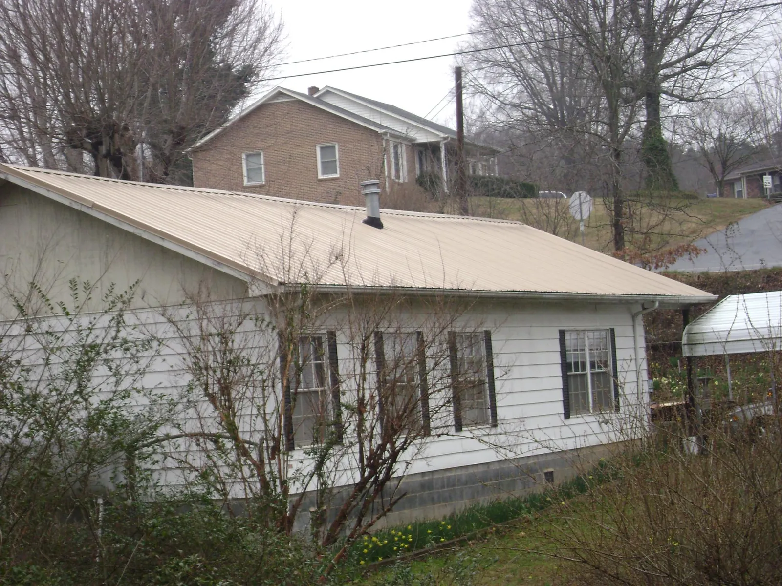 Tan metal roof on a white sided house set into a hillside — Commercial Roofing by Roofing Brothers in Klamath River